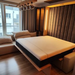 MEB-MAJSTER DAWID BIESZKE - Rozłożone łóżko w szafie z tapicerowanym wezgłowiem i oświetleniem LED, widok na okno z dekoracyjną gwiazdą. Nowoczesny design, jasne wnętrze.