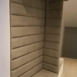 Tapicerowane siedzisko wnękowe z poziomymi przeszyciami, wbudowane w białą zabudowę meblową.