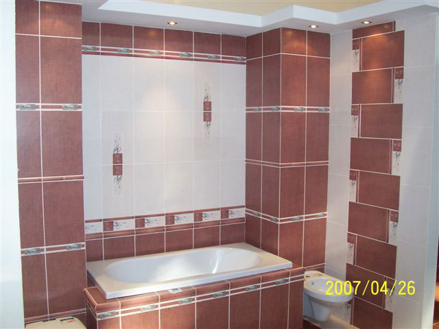 Wykończona łazienka z brązowo-białymi płytkami, zabudowaną wanną i podwieszanym sufitem z oświetleniem punktowym.