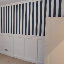 Pokój po malowaniu z białymi panelami ściennymi i granatowo-białymi pasami na górnej części ściany, widoczne ślady prac na podłodze, otwarte białe drzwi.