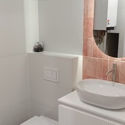 RC usługi ogólnobudowlane - Nowoczesna łazienka z białą ceramiką, umywalką nablatową na szafce z frezowanymi frontami i lustrem w różowej ramie z płytek. Minimalistyczny design.