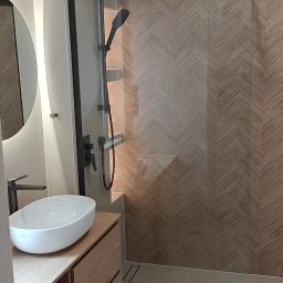 RC usługi ogólnobudowlane - Nowoczesna łazienka z kabiną typu walk-in, drewnopodobnymi płytkami w jodełkę, umywalką nablatową i szafką z jasnego drewna. Minimalistyczny design, czarne elementy armatury.