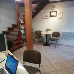 Biuro z drewnianymi schodami, stolikiem i krzesłami dla klientów, laptopem na biurku i certyfikatami na ścianie.