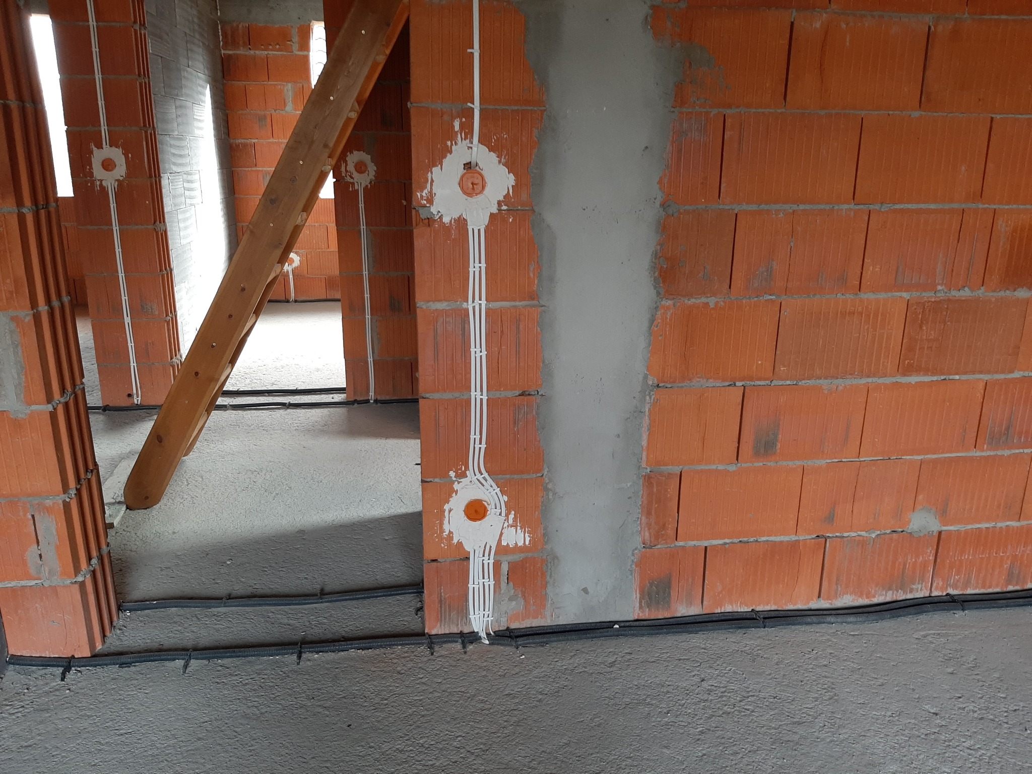 Wnętrze w surowym stanie w Bystrej z widocznymi przewodami elektrycznymi poprowadzonymi po ścianach z czerwonej cegły i w podłodze przed wylaniem posadzki.