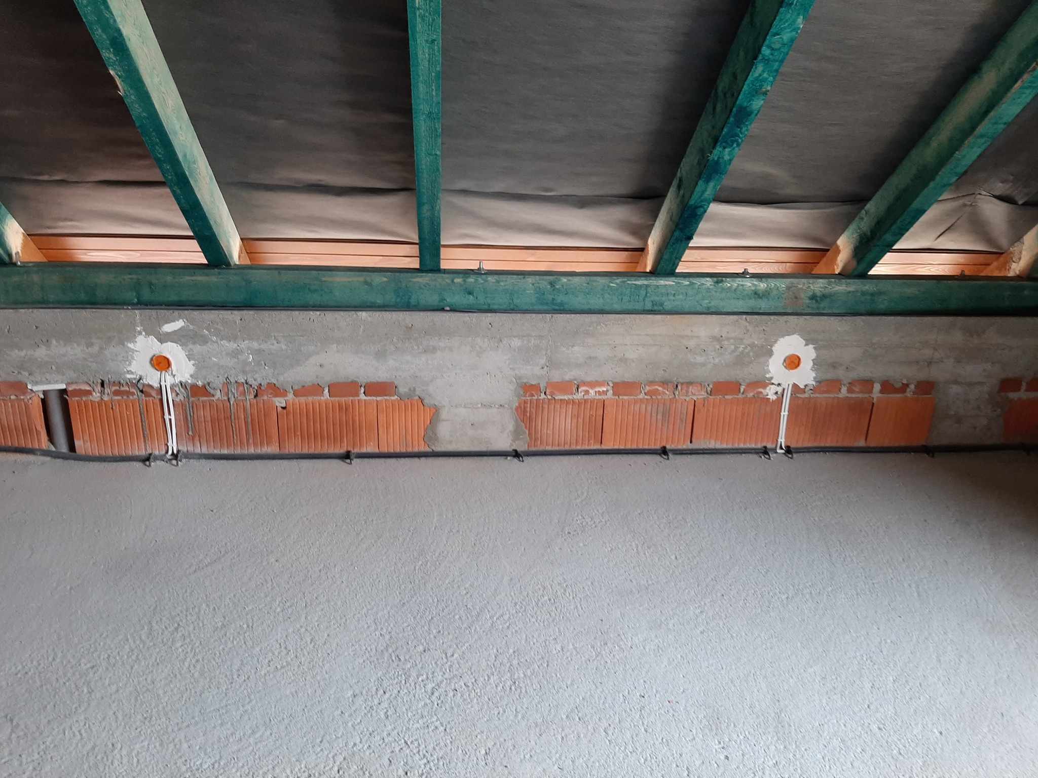 Surowy stan poddasza z widocznymi pustakami ceramicznymi, przewodami elektrycznymi wychodzącymi ze ściany i elementami konstrukcji dachu z impregnowanego drewna.