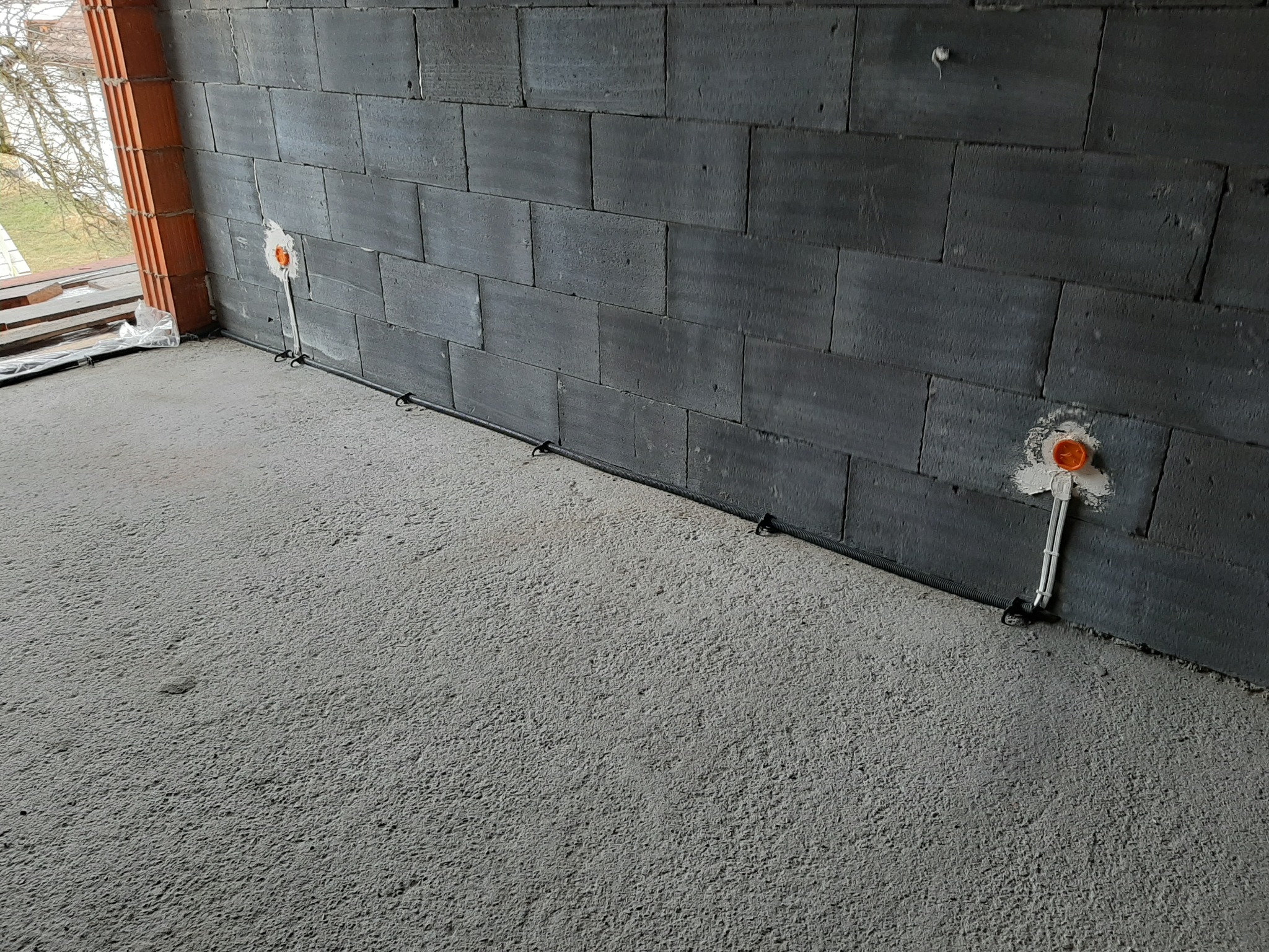 Surowy stan: przewody elektryczne wystające ze ściany z pustaków, przygotowane do montażu gniazdek, widoczne kable prowadzone wzdłuż ściany.