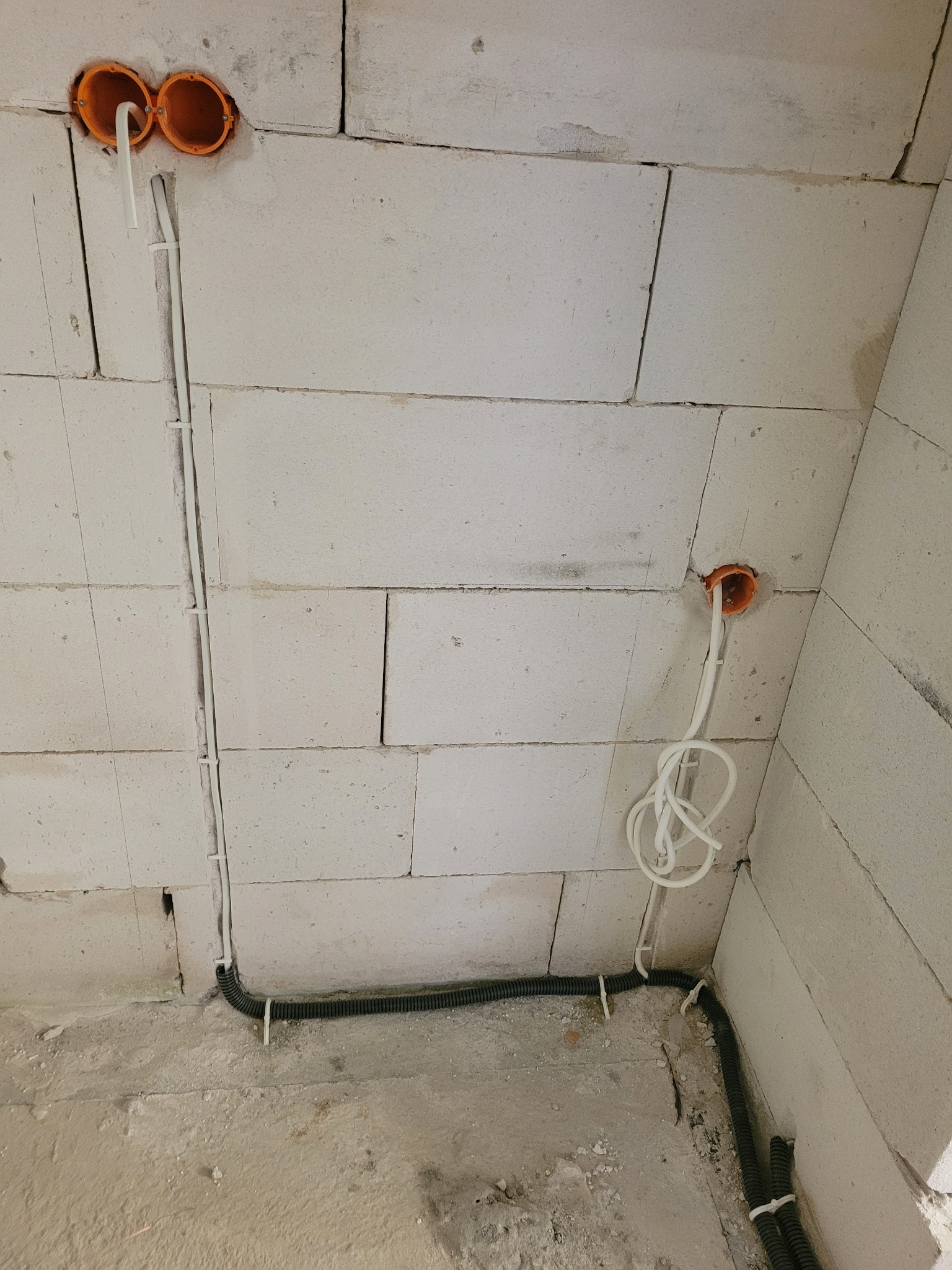 Surowy stan instalacji elektrycznej wewnątrz budynku: widoczne puszki instalacyjne, przewody elektryczne mocowane do ściany z betonu komórkowego oraz peszel przy podłodze.
