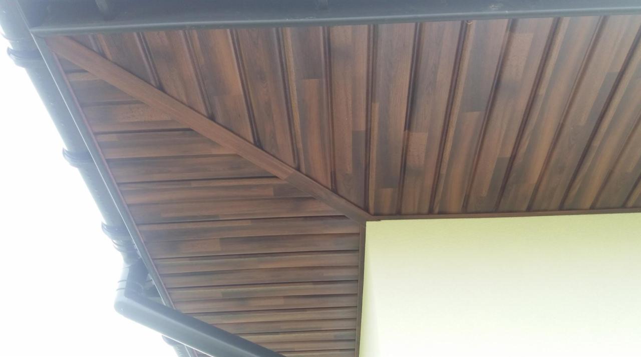 Podbitka dachowa z paneli imitujących drewno, widoczny fragment orynnowania i narożnik budynku z jasną elewacją.