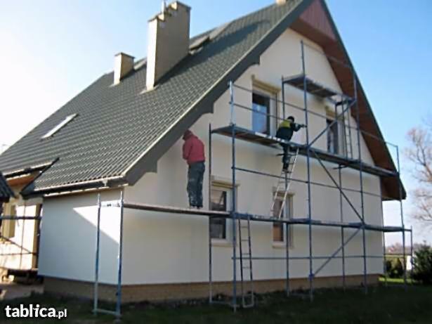 Dwóch pracowników na rusztowaniu przy ocieplaniu elewacji domu jednorodzinnego w Niedrzwicy Dużej, jeden maluje, drugi nakłada tynk, widoczna świeżo otynkowana ściana.