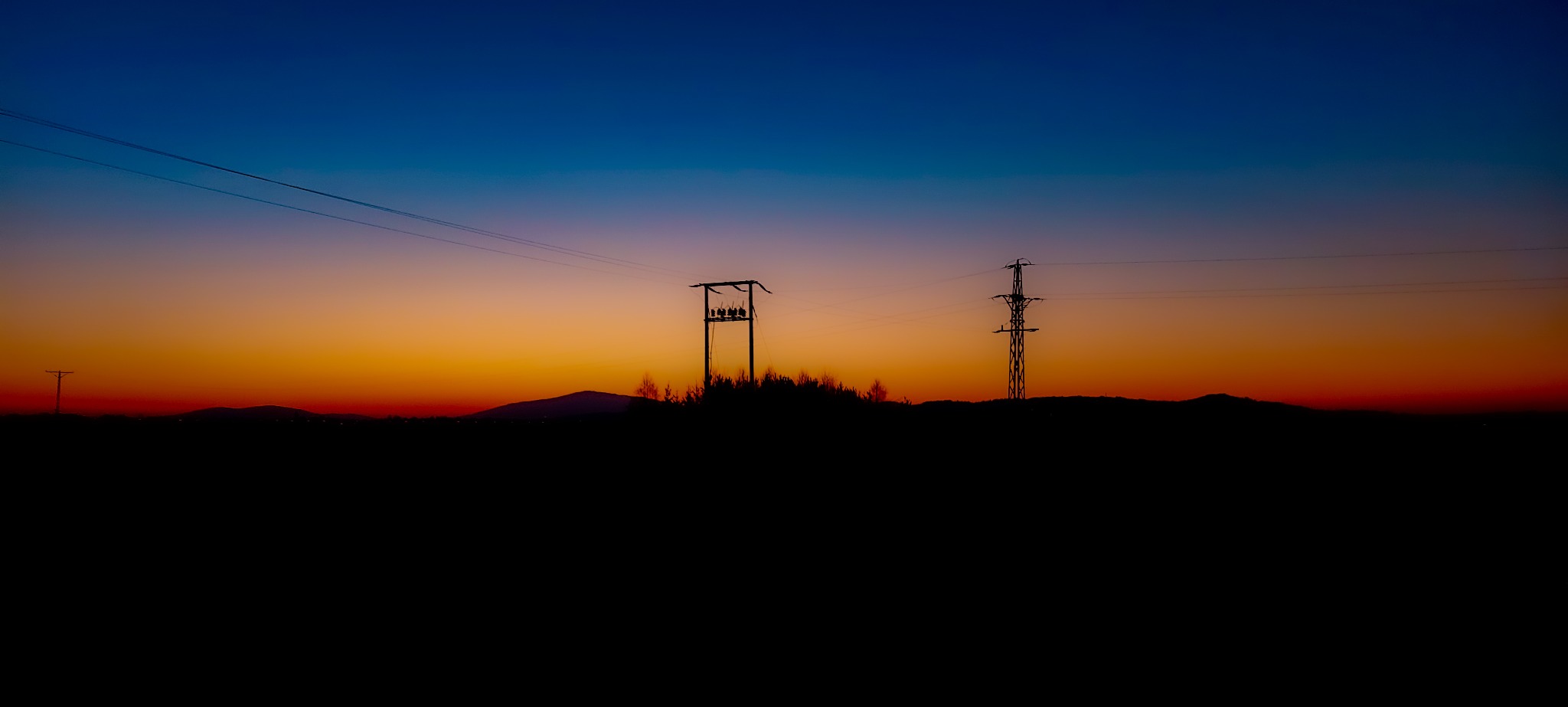 Sylwetki słupów energetycznych i linii wysokiego napięcia na tle gradientu kolorów nieba o zachodzie słońca, z ciemnym pierwszym planem.