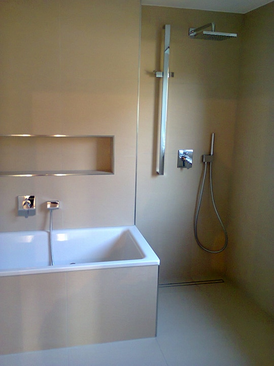 Wykończona łazienka z beżowymi płytkami, białą wanną i chromowaną armaturą, widoczny odpływ liniowy w podłodze.