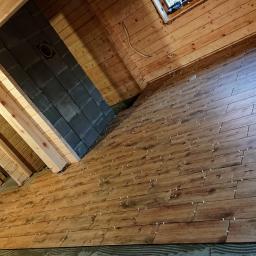 Company - Układanie drewnopodobnych płytek na podłodze w drewnianym domu, widoczne krzyżyki dystansowe i poziomica.