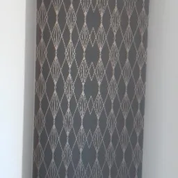 Ściana w Tomaszowie Lubelskim z szarą tapetą w geometryczne, złote romby, widoczna z bliska w narożniku pomieszczenia.