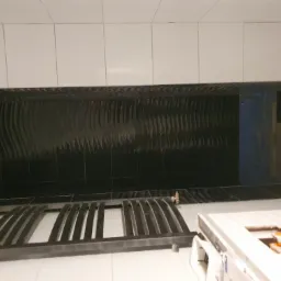 Łazienka w trakcie remontu: białe płytki na górze, czarne płytki z falistym wzorem na dole, widoczna rama prysznicowa i fragment maszyny do cięcia płytek.