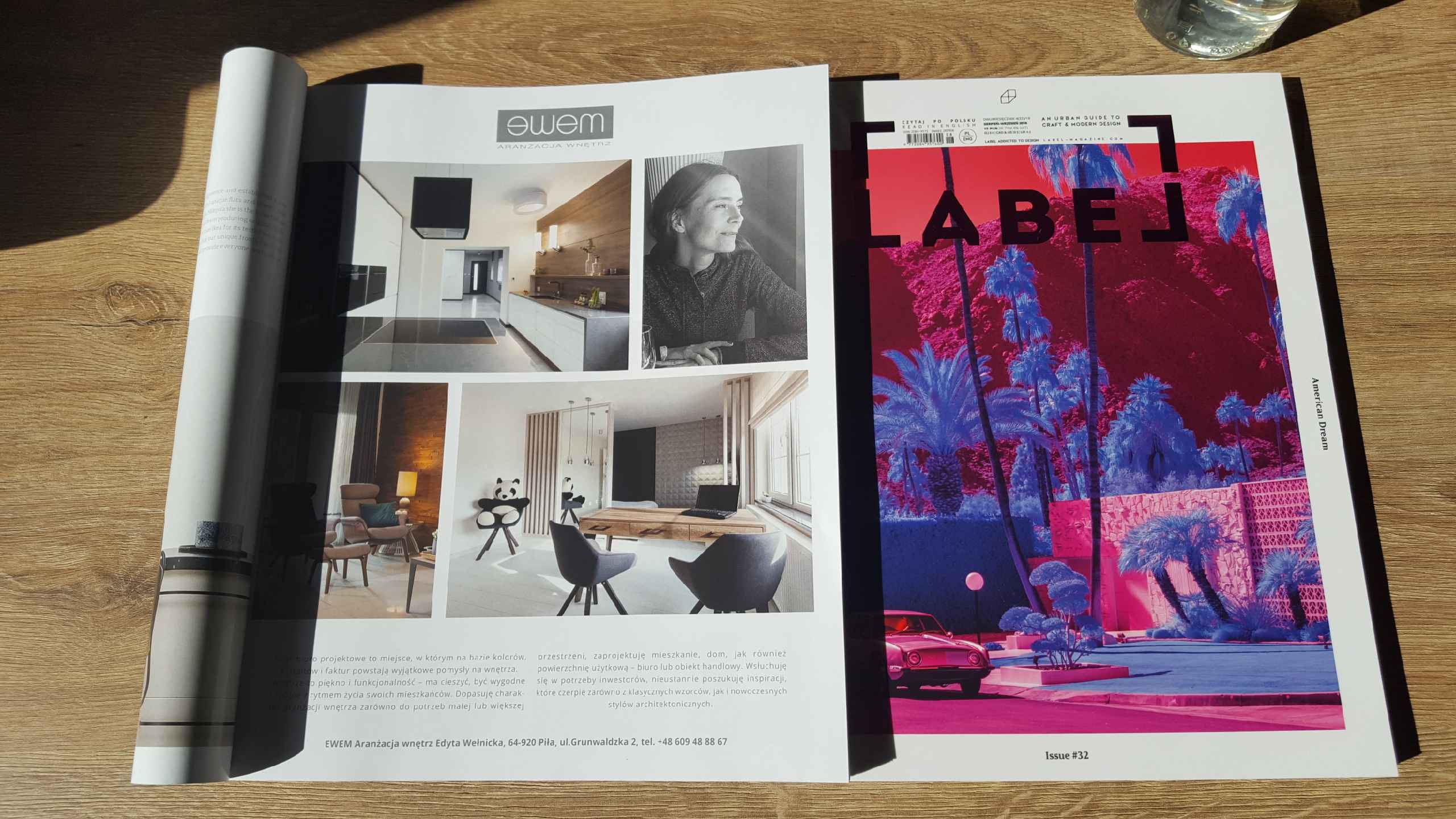 Rozłożony magazyn wnętrzarski na drewnianym stole, prezentujący zdjęcia aranżacji wnętrz, w tym kuchni i pokoju dziennego z pluszowym pandą na krześle oraz okładkę innego magazynu z motywem palm...