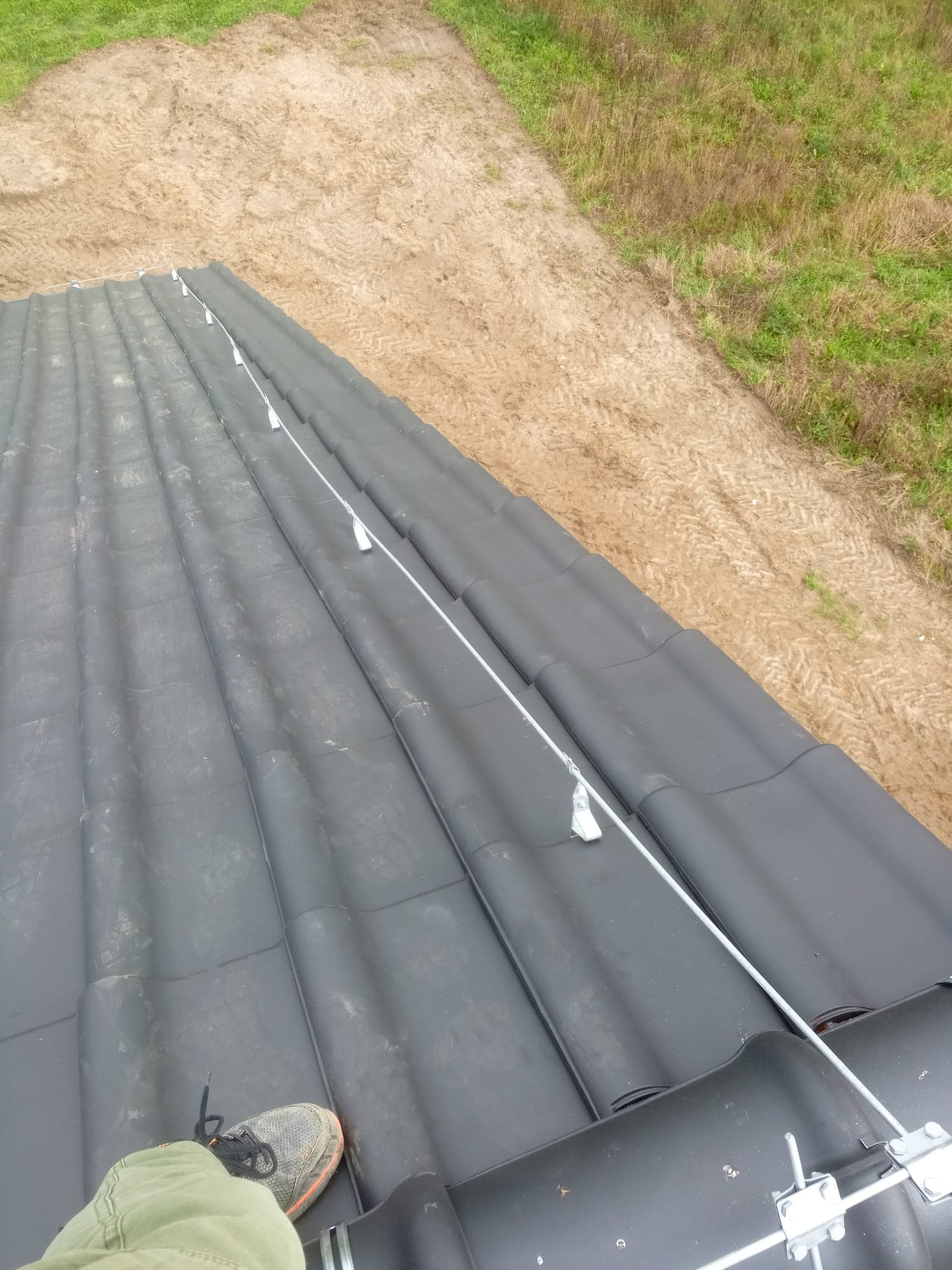 Czarny dach z dachówki ceramicznej z zamontowanym systemem odgromowym, widok z góry, teren wyrównany w tle.