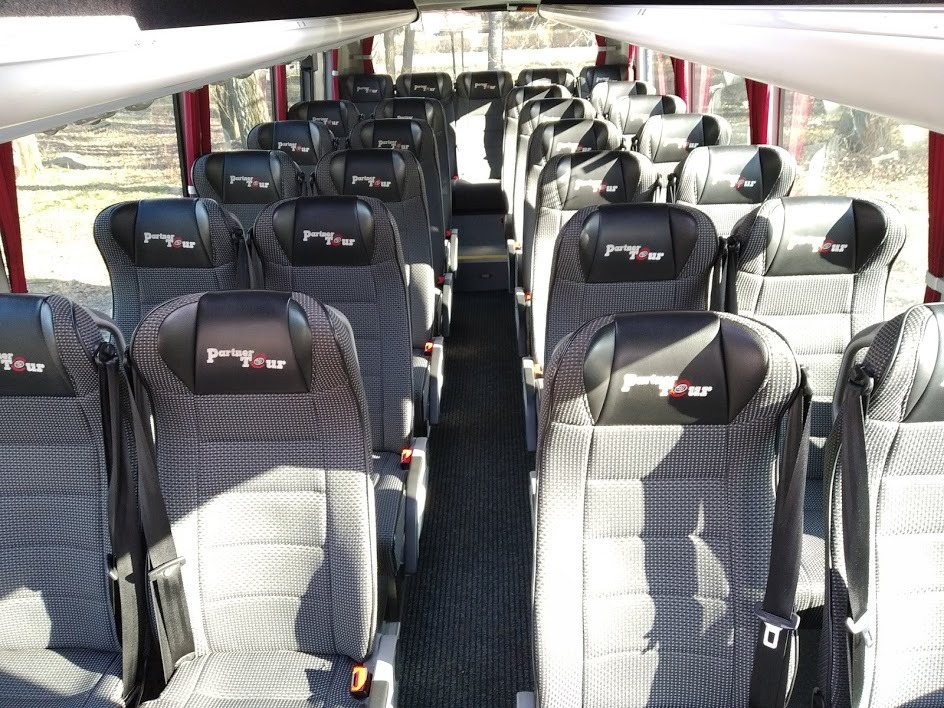 Wnętrze autobusu turystycznego z rzędami szarych siedzeń z logo Partner Tour na zagłówkach, widok z przodu pojazdu.
