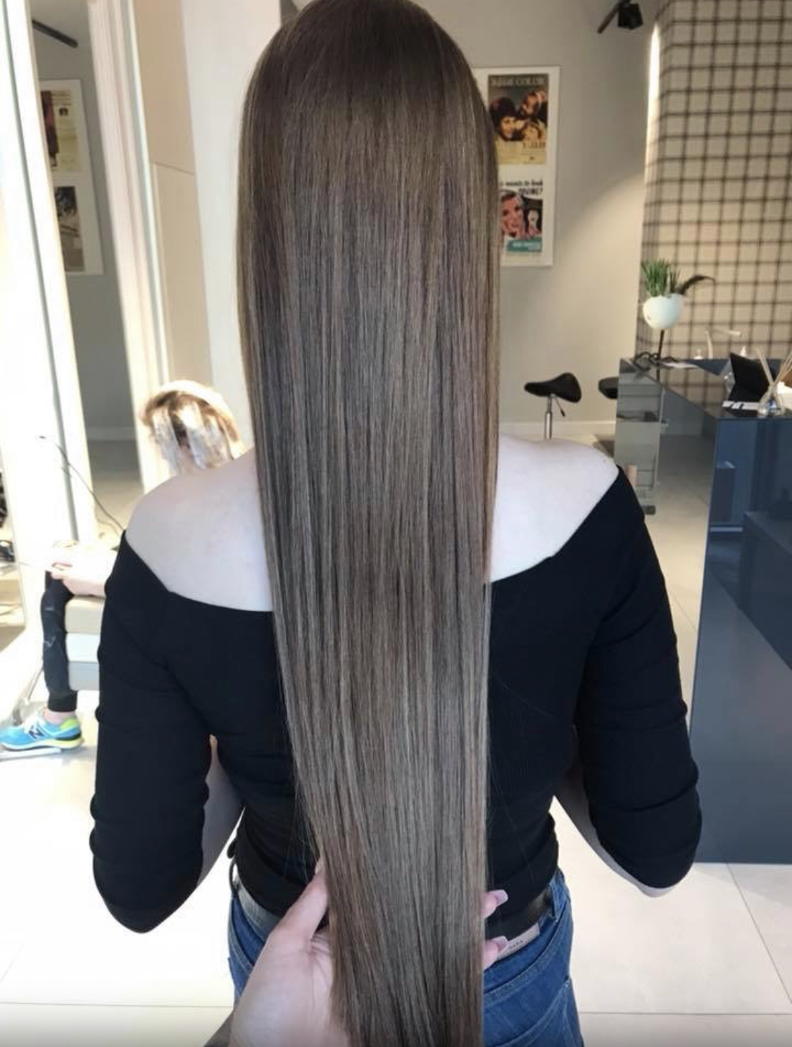 Długie, proste włosy w odcieniach brązu i blondu, z delikatnymi refleksami, widoczne z tyłu na tle salonu.