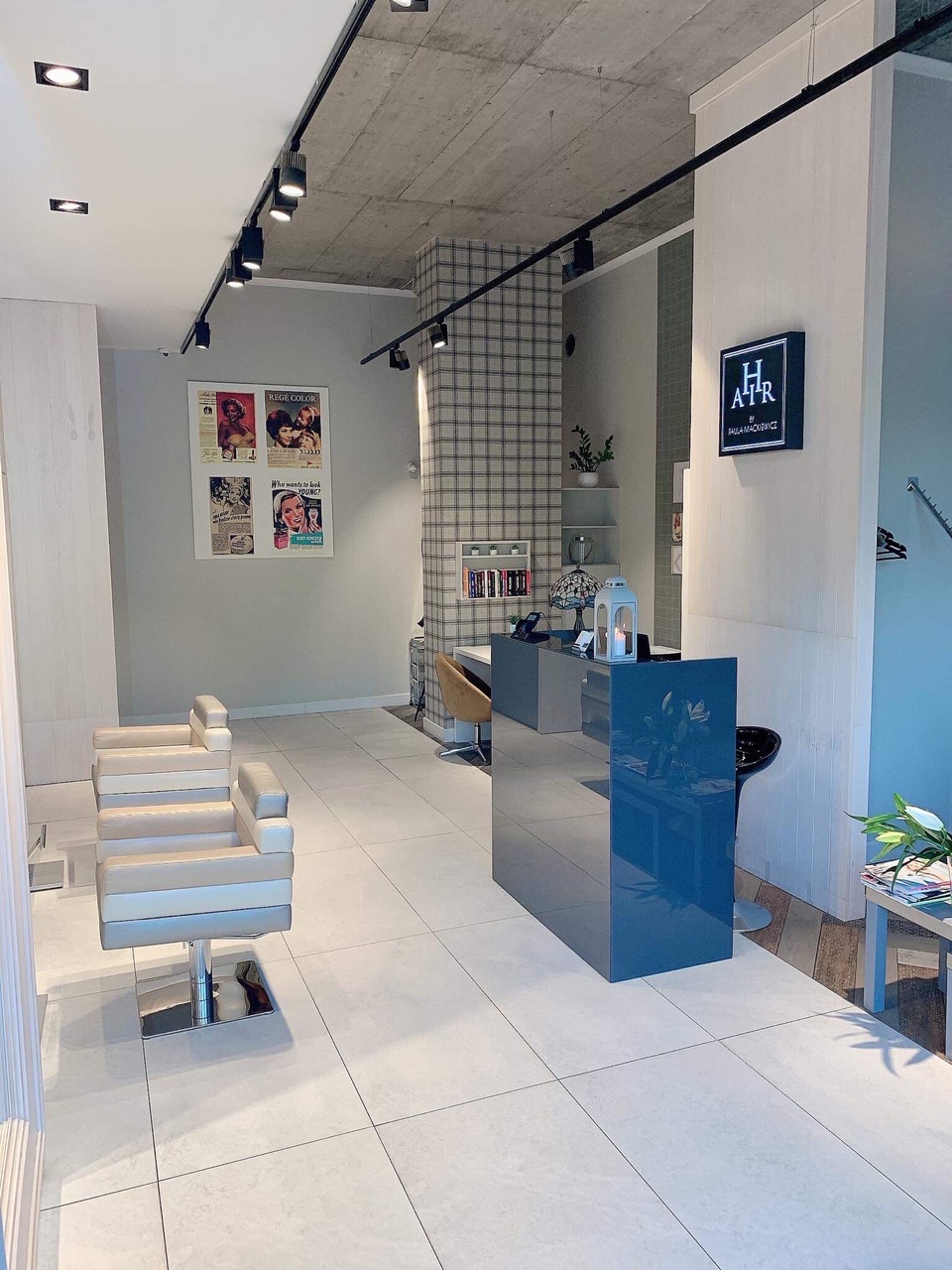 Nowoczesne wnętrze salonu z krzesłami dla klientów, recepcją z połyskiem i industrialnym oświetleniem sufitowym.