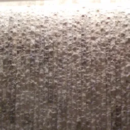 Ściana wyłożona nieregularnymi, pionowymi płytkami z jasnego kamienia naturalnego, oświetlona od góry, z fragmentem drabiny widocznym po prawej stronie.