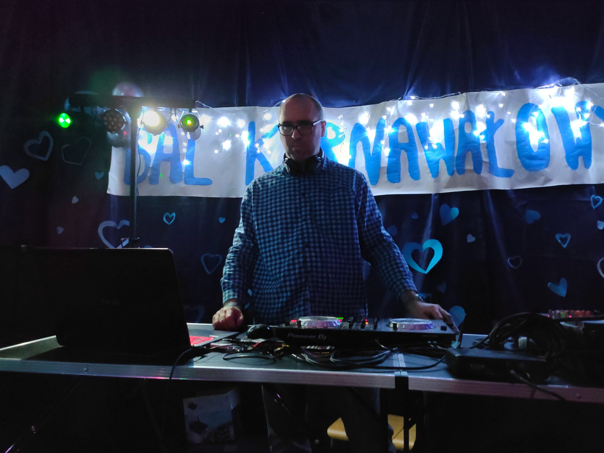DJ w trakcie występu na tle dekoracji z napisem 'SAL KARNAWAŁOWYCH' i motywem serc, oświetlenie sceniczne.