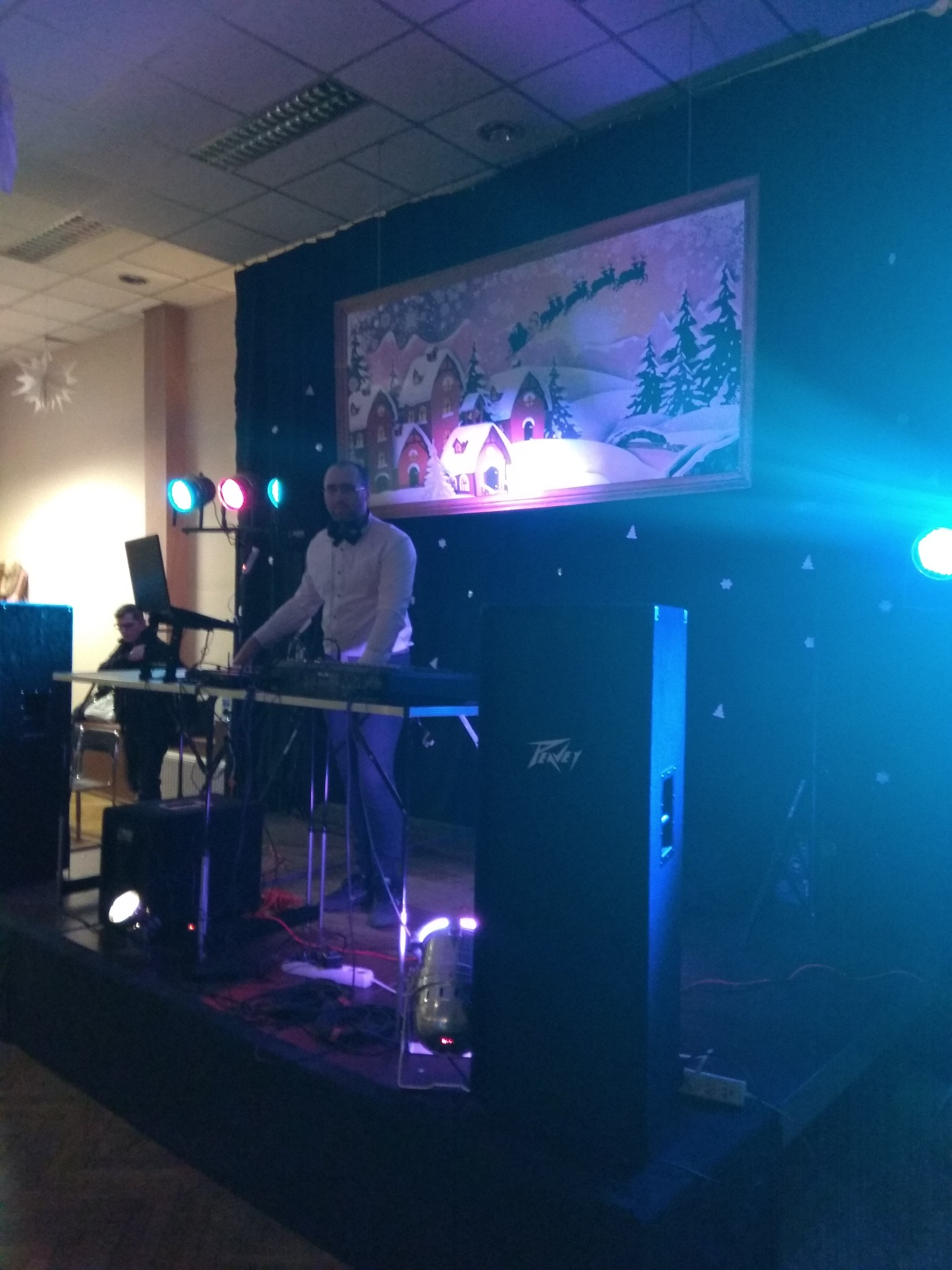 DJ w trakcie występu na scenie, oświetlenie sceniczne, dekoracja z motywem zimowym w tle.