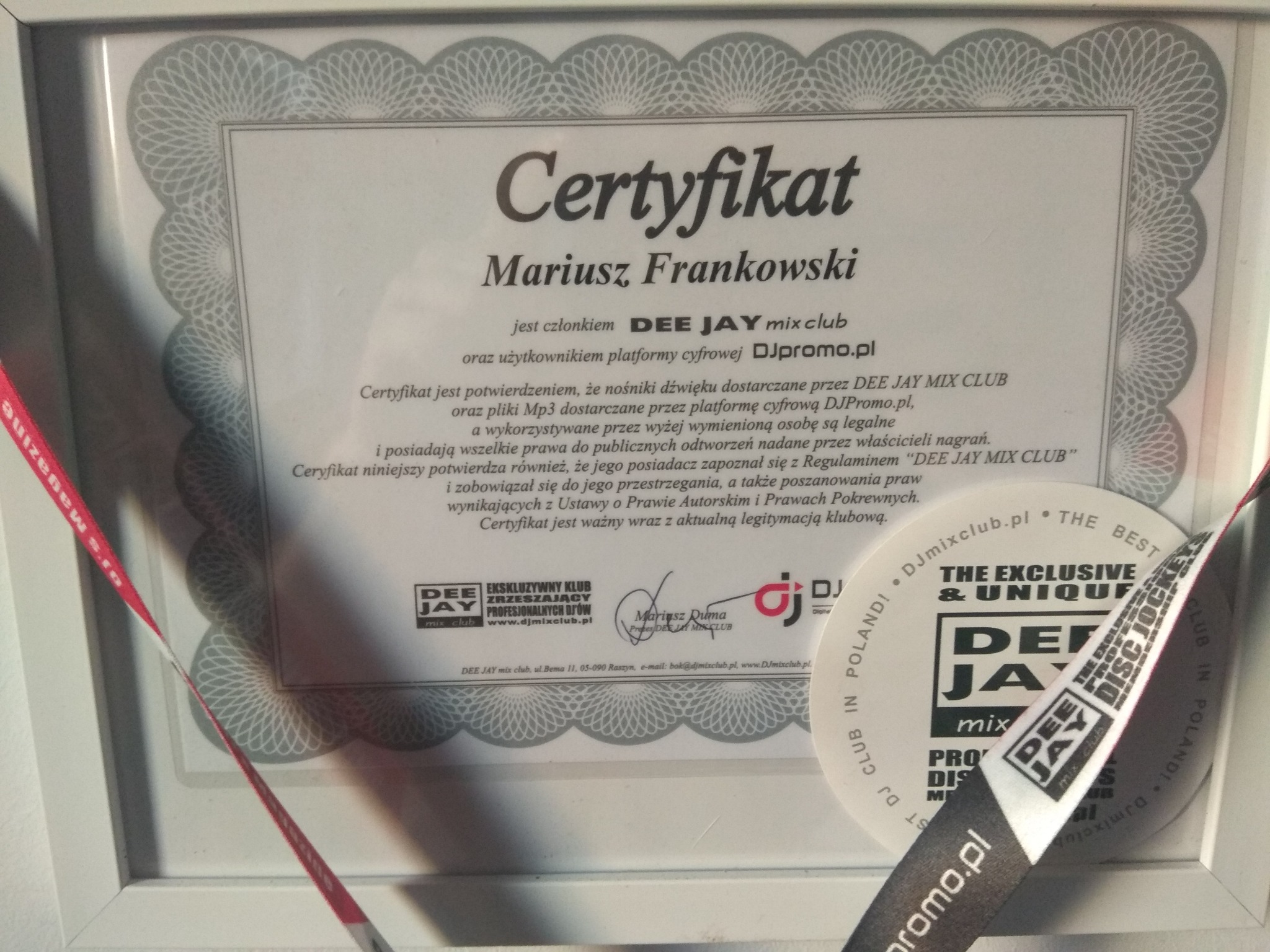 Oprawiony certyfikat Mariusza Frankowskiego z Dee Jay Mix Club, leżący obok klubowej smyczy DJpromo.pl i naklejki Dee Jay Mix Club.