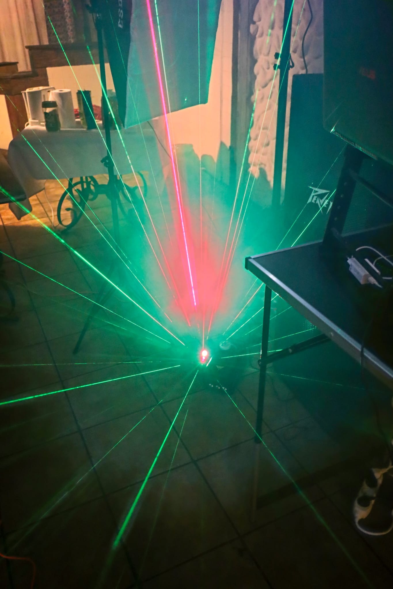 Zielone i czerwone promienie lasera rozchodzące się po podłodze podczas imprezy, widoczny sprzęt nagłośnieniowy marki Peavey oraz stolik z akcesoriami.