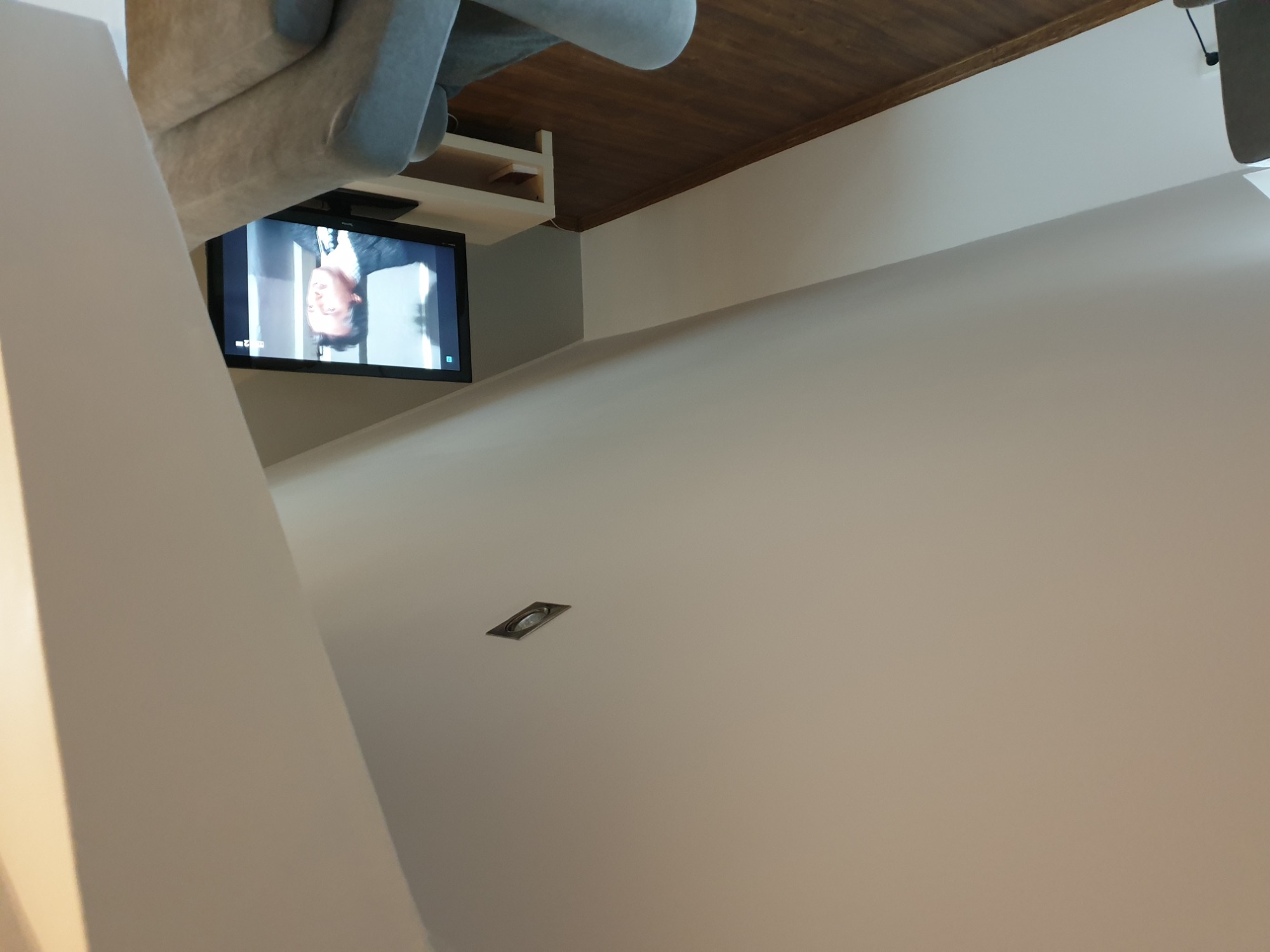 Jasne wnętrze z telewizorem zamontowanym na ścianie, widoczne fragmenty mebli i oświetlenie punktowe.