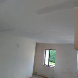 Pokój w trakcie prac przygotowawczych: ściany i sufit po nałożeniu pierwszej warstwy szpachli, widoczna drabina malarska.