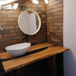 Nowoczesna łazienka w Trzemeśni z umywalką nablatową na blacie z żywicą, ceglana ściana i okrągłe lustro z oświetleniem.