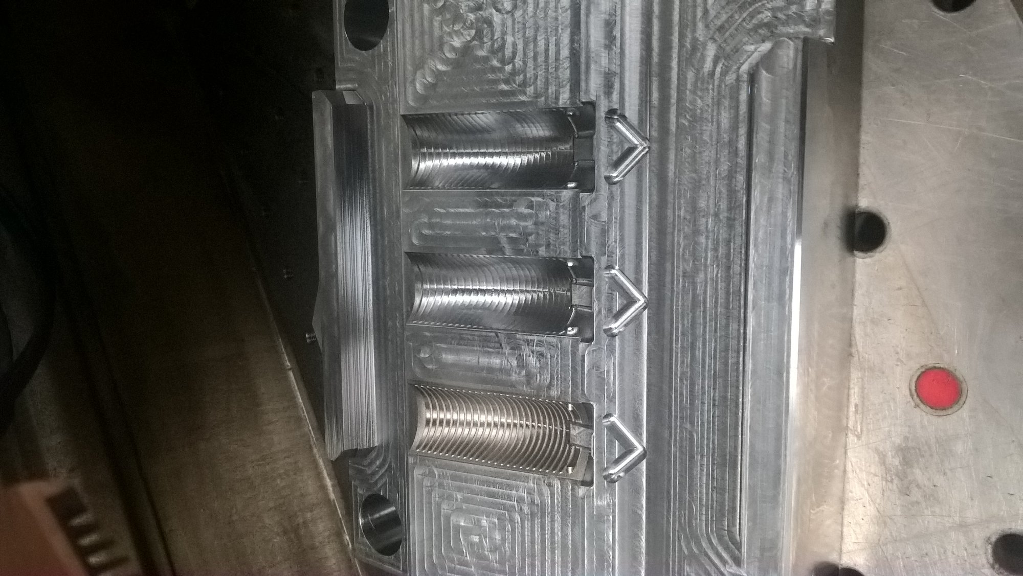 Metalowa forma z trzema półcylindrycznymi wgłębieniami o różnej fakturze powierzchni, przymocowana do metalowego bloku z widocznymi śladami obróbki.