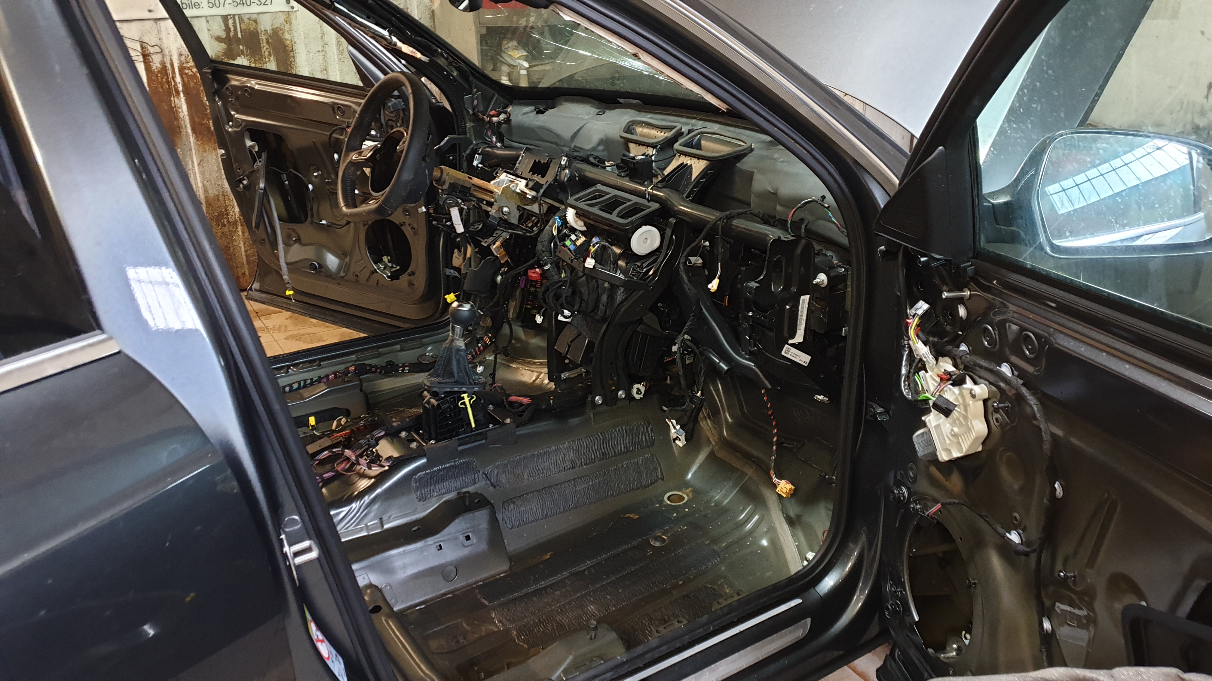 Wnętrze samochodu w trakcie demontażu deski rozdzielczej i elementów wyposażenia w warsztacie w Płocku, widoczne liczne kable i elementy instalacji elektrycznej.