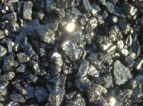 Góra błyszczących brył węgla kamiennego o nieregularnych kształtach, z widocznymi refleksami światła na powierzchni.