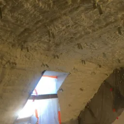 Aplikacja izolacji piankowej na poddaszu w Ciechanowie, widoczne metalowe mocowania i folia ochronna na oknie dachowym.