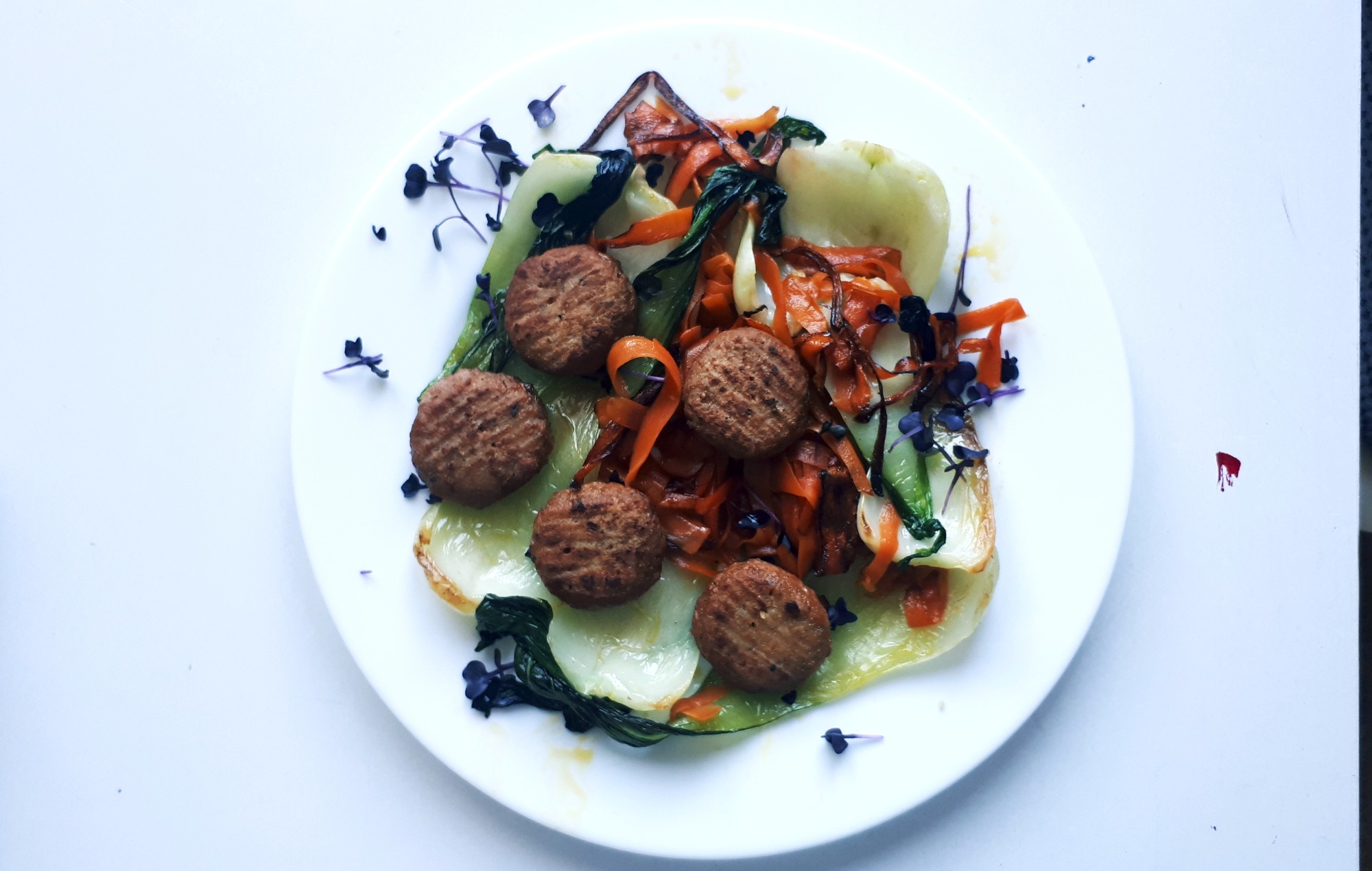 Elegancko podane danie wegetariańskie na białym talerzu: kotleciki roślinne, podsmażany pak choi, marchewka julienne i mikro zioła.