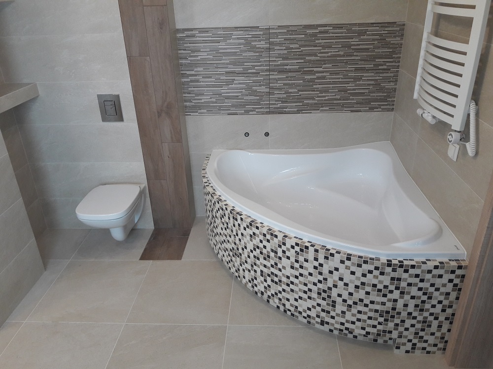 Nowoczesna łazienka z narożną wanną obłożoną mozaiką, wiszącą toaletą i grzejnikiem drabinkowym na ścianie z poziomymi paskami dekoracyjnymi.