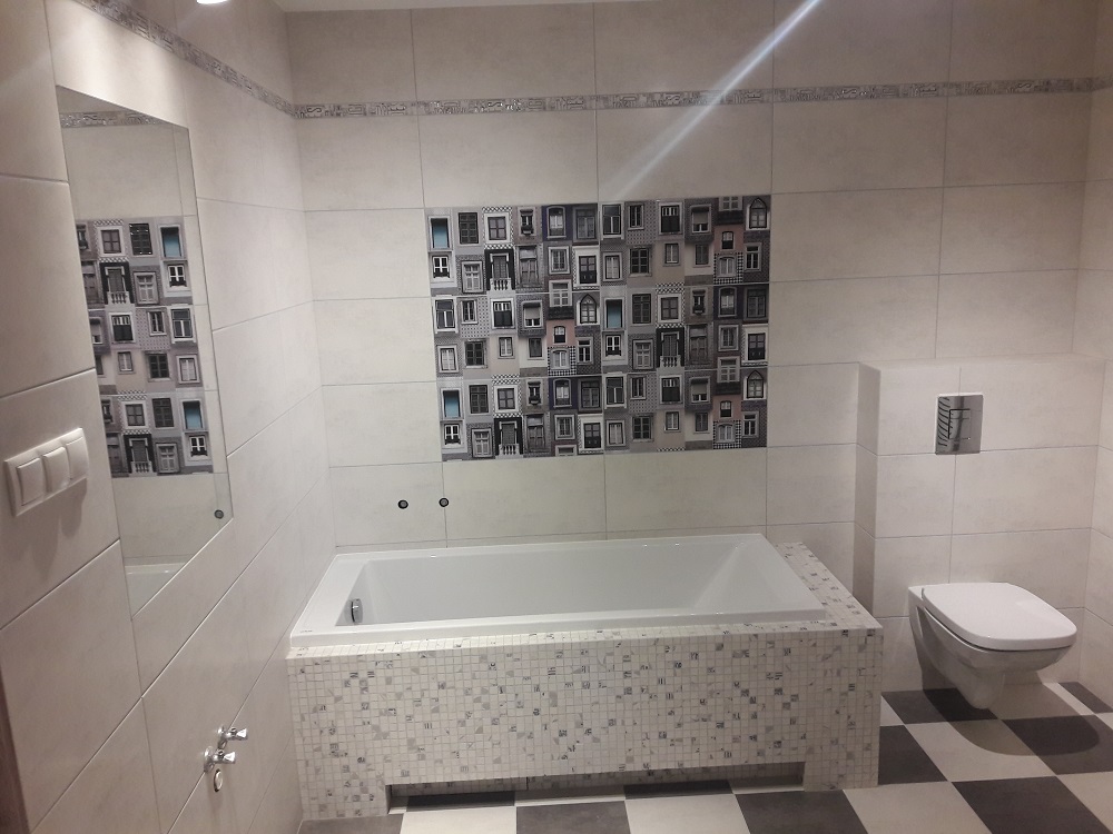 Wykończona łazienka w Krępcu z wanną obudowaną mozaiką, białą armaturą i płytkami imitującymi okna na ścianie.