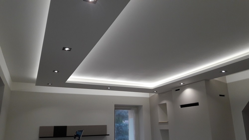 Nowoczesny sufit podwieszany z oświetleniem LED w jasnym pomieszczeniu z widocznym oknem i elementami dekoracyjnymi na ścianie.