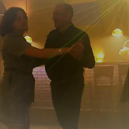 Para tańcząca na parkiecie oświetlonym laserami, w tle widoczne dekoracyjne lampy i inni uczestnicy zabawy.