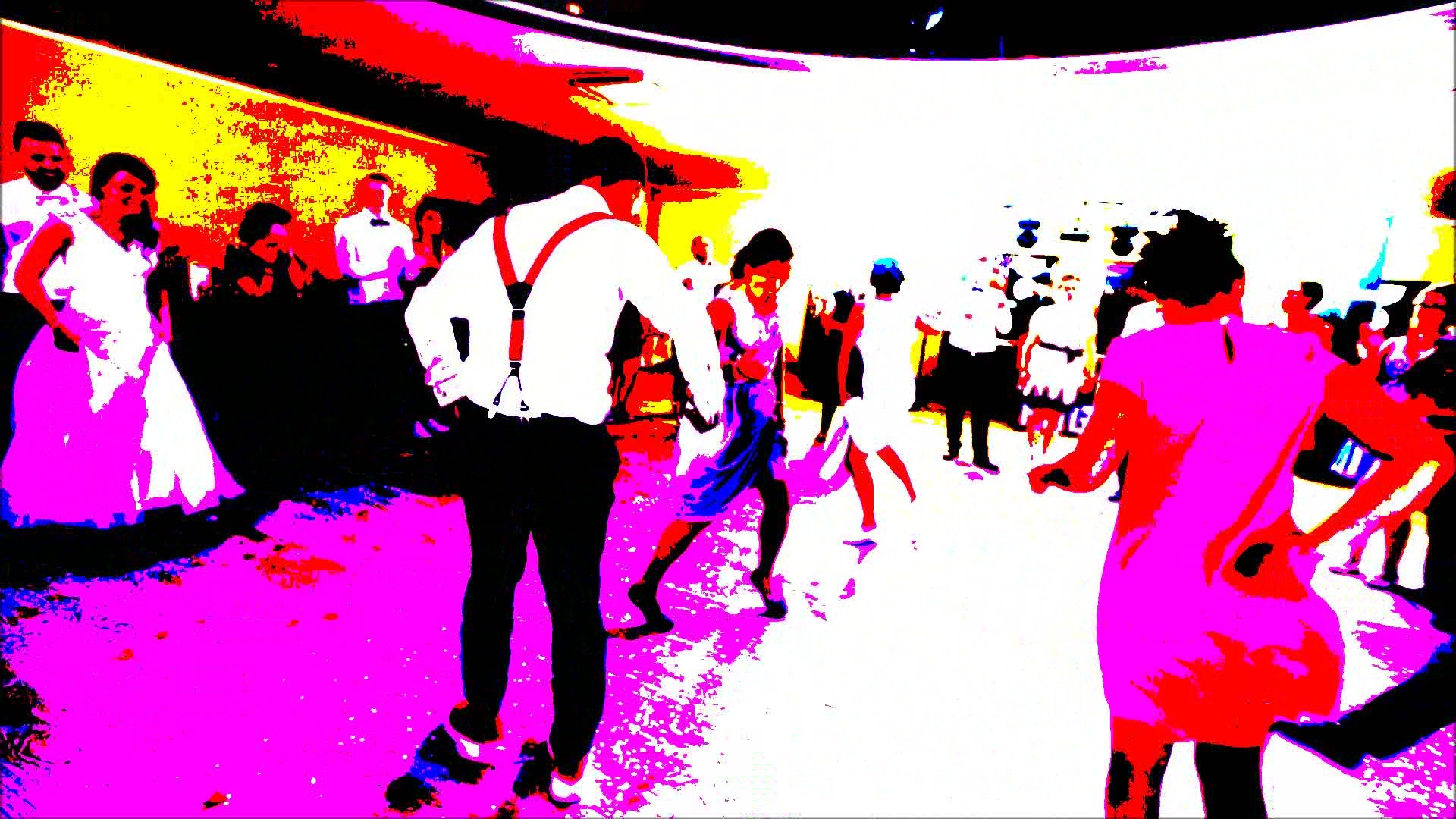 Para w tańcu na parkiecie podczas imprezy, mężczyzna w szelkach, w tle goście weselni.