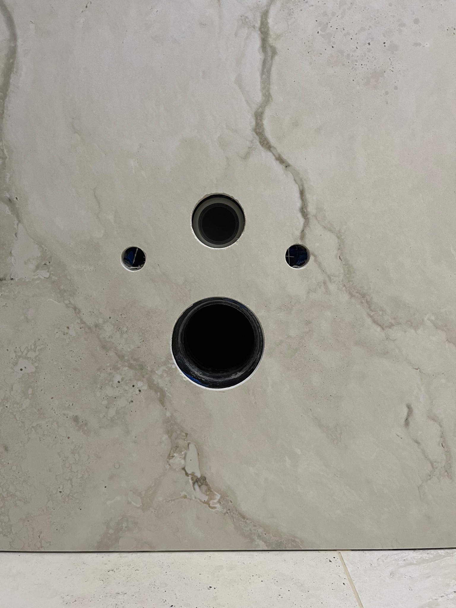 Płyta z jasnego marmuru z wywierconymi otworami na armaturę łazienkową, widoczne przewody instalacji.