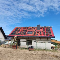 TOMASZ TOMCZAK TOM-BUD - Budowa domu jednorodzinnego z częściowo ułożoną dachówką ceramiczną w kolorze czarnym i czerwonym na czerwonej membranie dachowej, widoczne okna dachowe, komin i drewniana drabina oparta o dach,...