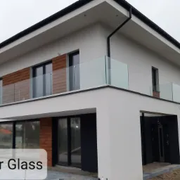 Nowoczesny dom jednorodzinny z balkonami zabezpieczonymi szklanymi balustradami, widok z zewnątrz w pochmurny dzień.