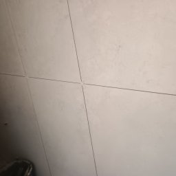 Łukasz Trusiak Zakład Ogólnobudowlany - Jasne, prostokątne płytki ceramiczne z delikatną teksturą układane na ścianie, z widocznymi białymi krzyżykami dystansowymi w fugach.