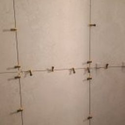 Łukasz Trusiak Zakład Ogólnobudowlany - Układanie jasnych, matowych płytek ściennych z precyzyjnym systemem poziomowania, gdzie widoczne są klipsy i kliny zapewniające równe spoiny.
