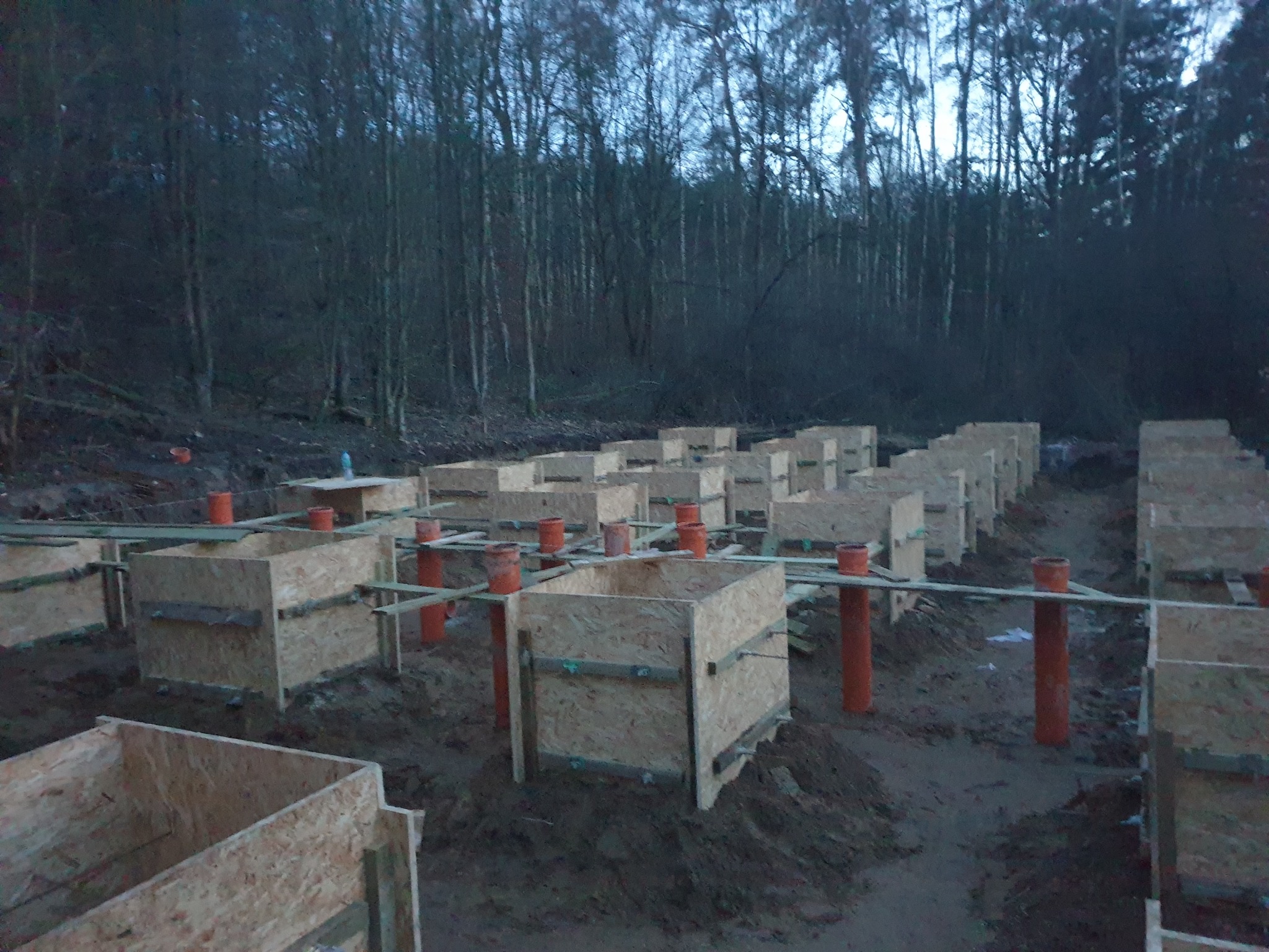 Szczegóły fundamentów pod dom modułowy w Chrzypsku Wielkim. Widoczne drewniane szalunki i pomarańczowe rury w ziemi, przygotowane pod wylewkę.