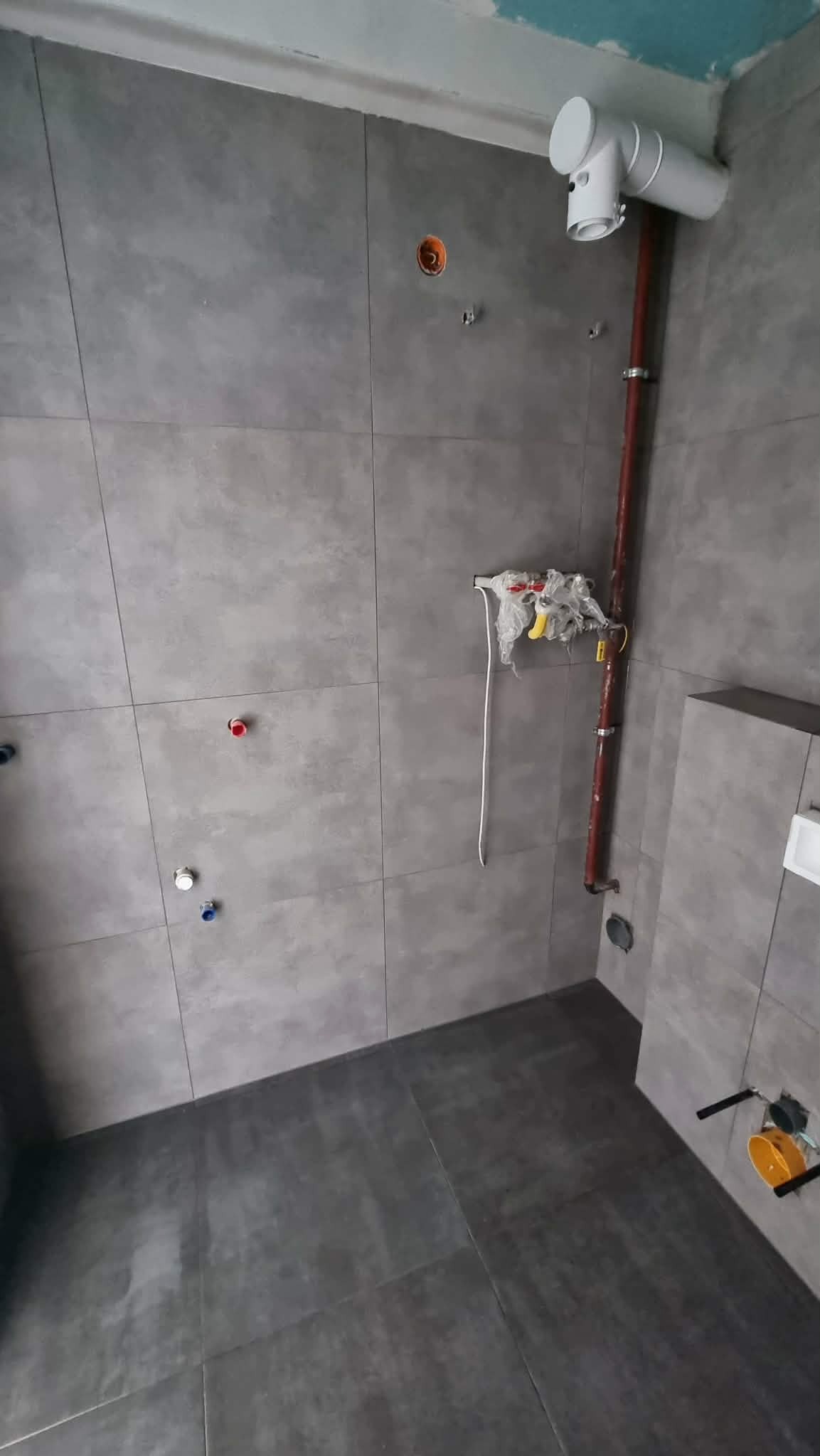 Szare płytki w łazience w Chrzypsku Wielkim, widoczne rury i instalacje wodne. Minimalistyczny design, surowy styl wykończenia wnętrz.