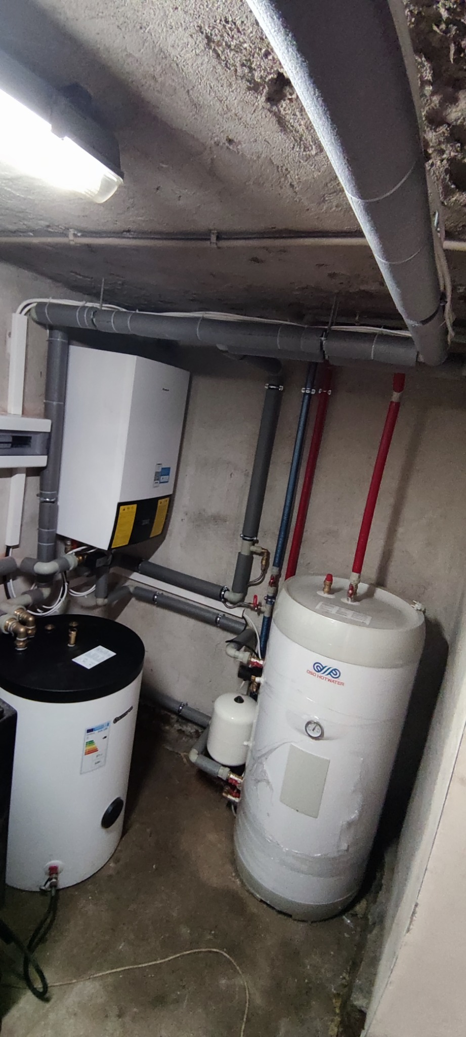 Instalacja grzewcza w piwnicy z dwoma zbiornikami, piecem gazowym kondensacyjnym, rurami izolowanymi termicznie, manometrem i przewodami doprowadzającymi wodę, widok z dołu.