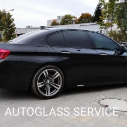 Czarne BMW serii 5 z przyciemnionymi szybami bocznymi i tylną, zaparkowane na betonowym placu, widok z tyłu na bok, z widocznym logo M Performance.